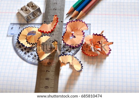 cell school notebook on which there are sharp colored pencils, pencil sharpener, ruler, protractor and sawdust 