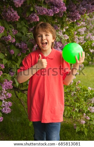 sporty happy smiling kid boy with green ball playing in the lilac flowers park outdoor alone
