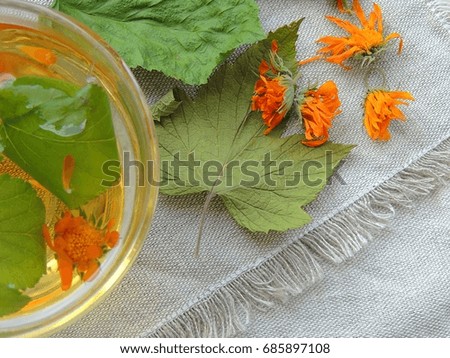 Healthy organic herbal tea with calendula and dry leaves of blackcurrant and mulberry. Calendula flowers, leaves, handmade linen towel. Top view.