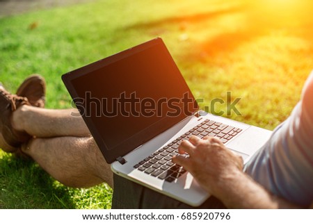 Cropped shot of man using laptop with blank screen while sitting on green grass