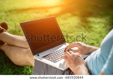 Cropped shot of man using laptop with blank screen while sitting on green grass