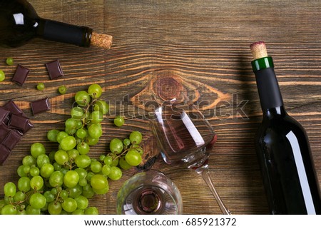 Red wine bottle, grape, chocolate and glasses over wooden table. Top view with copy space