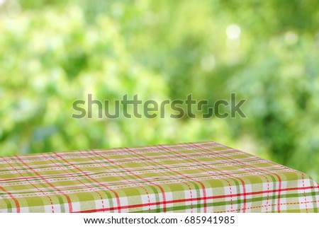 Empty table in the summer garden. The table is covered with a green checkered cloth. Green blurred background.