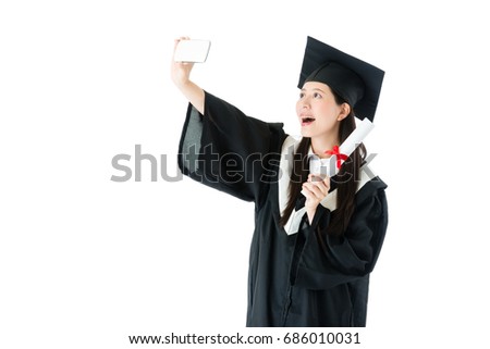 smiling beauty girl student getting diploma certificate and wearing graduation clothing using mobile cell phone taking photo selfie recording important time isolated on white background.