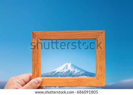 Hand hold wood frame and focus Fuji mountain on background. image look like photo on the frame. nature wallpaper and background. 
