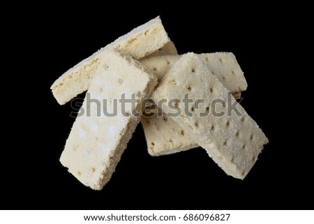 Piles of shortbread biscuits isolated on a black background and centred in the image. The biscuits are sugar coated and covered in crumbs.