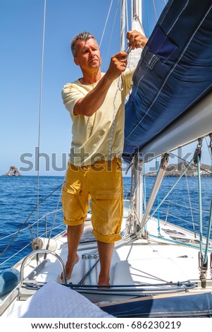 Adult man working on sailboat, tying a knot on the the ropes on  sails of the yacht, sailor yachtsman controlling the sail on sailing boat. Yachting sport activities and sailing Royalty-Free Stock Photo #686230219