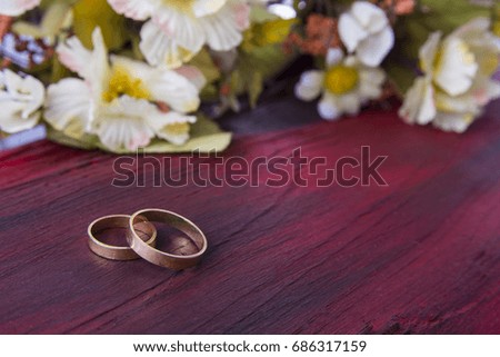 Wedding rings on the red wood background with flowers