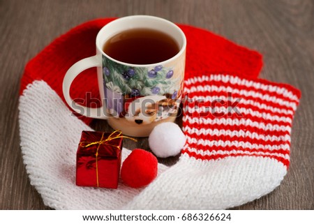 Tea and New Year. Image of a dog in a Santa Claus hat on a tea mug. A cup of tea, wrapped in a knitted scarf, creates a cosiness for the new year. The dog's figure symbolizes the year of the dog.