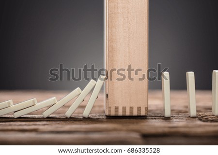 Closeup of wooden block amidst falling and upright domino pieces on table against gray background