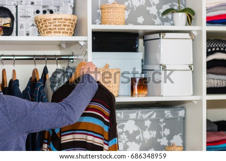 The European blond boy teenager brings wardrobe order, puts everything in its place, hides things in boxes. Wardrobe with women's, men's and child's clothing. Closet. Royalty-Free Stock Photo #686348959