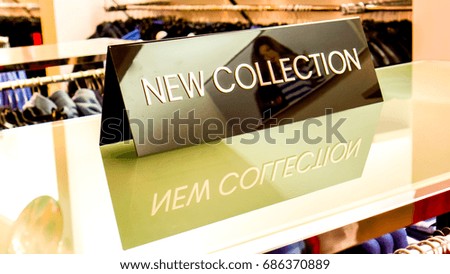 glass shelve and black plate with reflection. medium triangle black plate in a clothing store with a sign NEW COLLECTION on glass shelf against white wall with light reflections