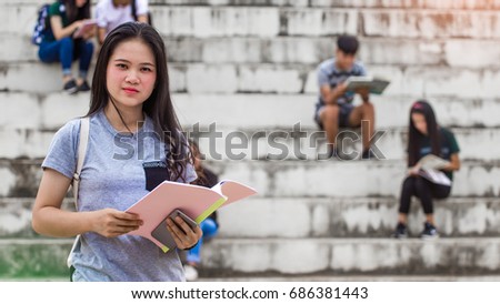 happy young girl student holding smart phone and book,at high school outdoors