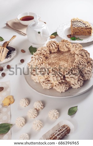 Beautifully decorated dessert table where the cake with meringue, layered pieces of cake and Cup of tea on a white table. Arrangement of delicious sweets, top view