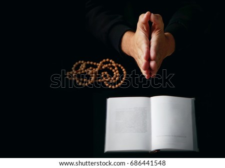 Male hand folded in prayer rosary beads closeup and koran on background.
