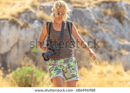 Caucasian young hiker during a trekking on a blurred landscape. Traveler woman photographer with professional camera outdoor. Female photographer walking in nature. Adventure and leisure concept.