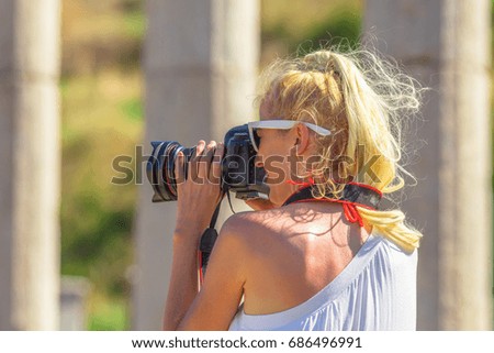 Profile of blonde caucasian woman photographer with professional camera in Ancient Messene, Archaeological Site, Peloponnese, Greece. Close up of female shotting a blurred ruins.Europe travel holidays