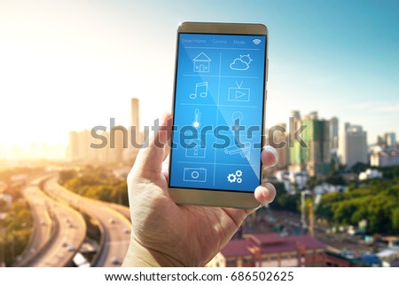 Smart remote home control system apps on a hand phone with out of focus cityscape background.