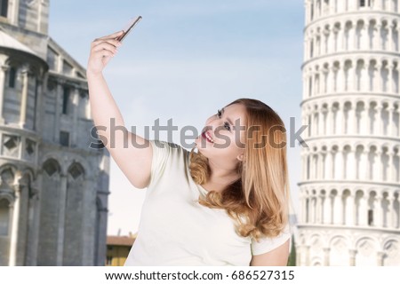 Portrait of happy woman taking selfie photo by using smartphone in front of pizza tower 