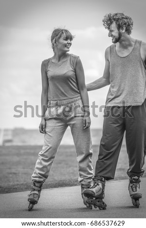 Love romance sport fitness leisure concept. Teen couple together on skates. Girl and boy riding rollerskates in coastal park. Black and white shot.