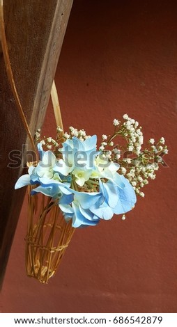 Soft blue Hydrangea and little white gypsophila  in small hanging bamboo basket on wooden wall.  Simple beautiful  flower arrangement.