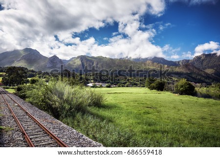 Greenery and railroad in Asturias. Picos de Europa mountains landscape in summer. Straight railway line surrounded by greenery.