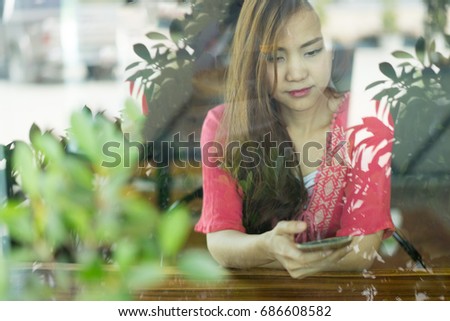 Asian woman use her smart phone to update her promotion on social network in coffee shop .  Take a photo through clear glass mirror.  Concept for digital nomad, independent location entrepreneur.