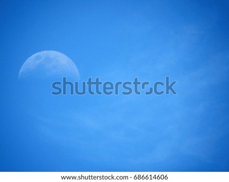 Half moon with top half lit in lightly clouded blue sky, seen from the equator 