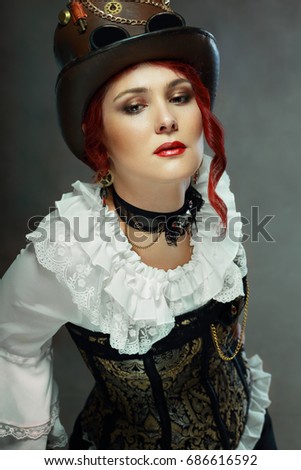portrait of beautiful steampunk woman wearing vintage hat and corset posing next to color background
