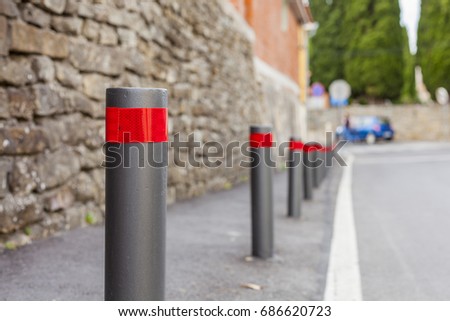 City road poles with the reflective stripe on a sidewalk with a car on a blurred background