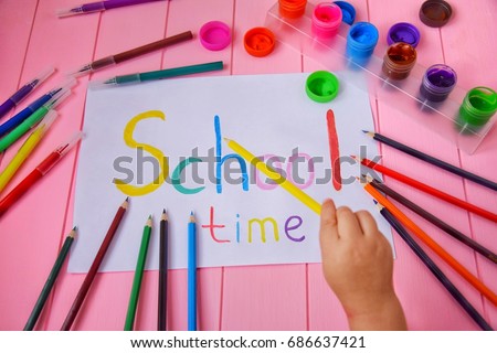 Poster School time. A child's hand draws with a pencil and paints. Color pencils, paints, felt-tip pens on a pink table.
