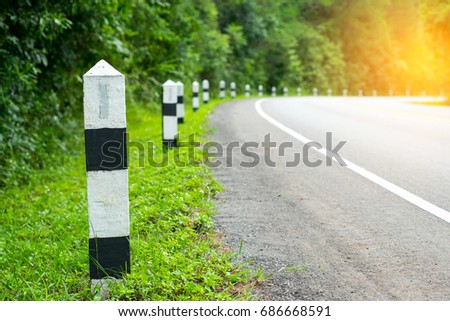 Black and white milestones with green grass roadside, Trees roadside in background . concept for next step. Next station.
