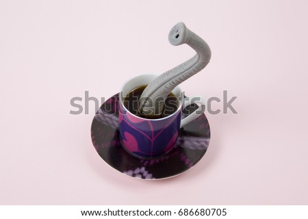 An elephant trunk emerging from a small design cup of coffee as if he were hiding. Minimal funny and quirky design still life photography