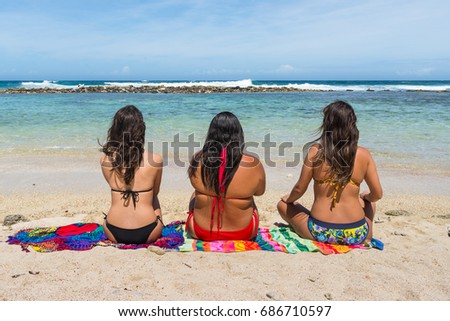 Three girls sitting on the beach facing towards the ocean. Location: Yapascua Bay, Caribbean Sea, Venezuela