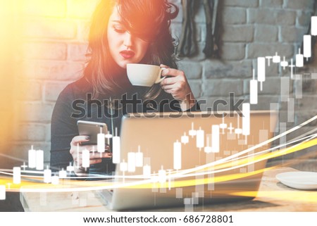 Young business woman is sitting in cafe at table,drinking coffee,working on laptop and using smartphone.In foreground are binary options charts.Hipster girl analyzes level of exchange sales.Marketing.