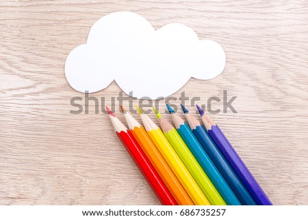 Paper cloud and rainbow rain from Seven pencils of rainbow colors lie on wooden table. Copyspace. Back to school. Wooden background.