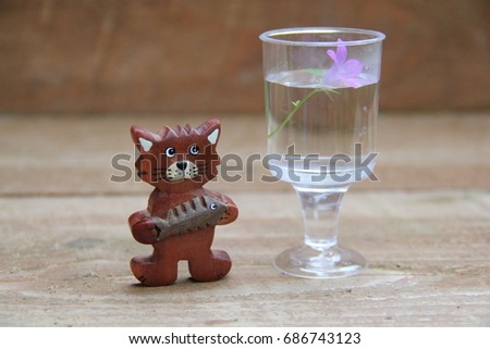 Cute decorative wooden cat with fish and a forest bell (Campanula patula) in a mini-glass of water.