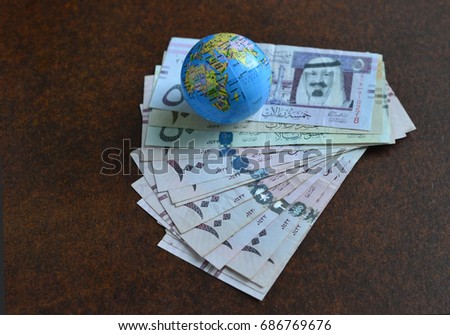Saudi Rials currency notes along with miniature globe sphere showing Saudi map- Stock image. Spread of Saudi Riyal currency notes.