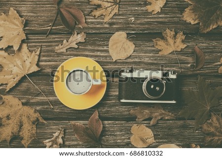 Autumn leaves, camera and coffee cup on wooden table. Photo in old color image style