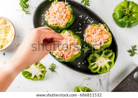 Autumn recipes. Home stuffed bell pepper with minced meat, carrots, tomatoes, herbs, cheese. Cooking process. White marble table. Top view. Woman add cheese on peppers. Female hands in picture.