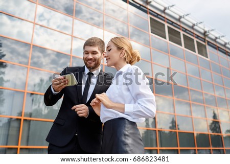 View from below - beautiful young girl freelancer and man designer in large firm talking during break and watching something in the tablet on background of office building