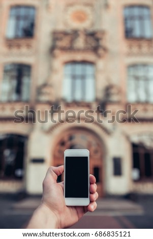 Taking white smart phone in hand on the background of building.