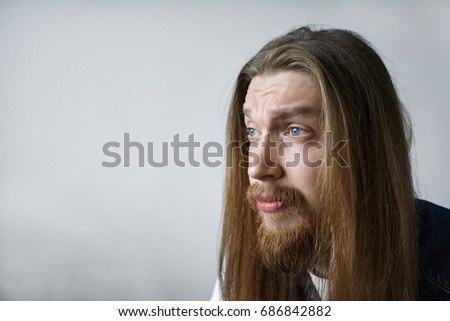 Portrait of handsome expressive bored unshaven young man with walrus moustache and messy hairstyle posing in studio, looking in front of him, dying of boredoom. Human facial expressions and emotions