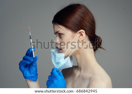 Young beautiful woman on gray background in medical glove holds syringe, plastic, medicine.