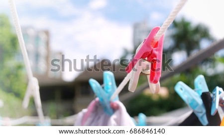 Soft, bright shot of vivid pink and white clothespins hanging freely on white rope among others used to clip clothes on sunny day with blurred house, garden and high rise as background