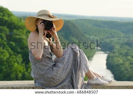 Girl in hat takes pictures against the background of green forest and river