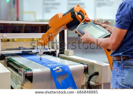 Engineers use a wireless remote control robot for gripping a workpiece out of the machine via a conveyor belt for smart factory, industry 4.0 concept