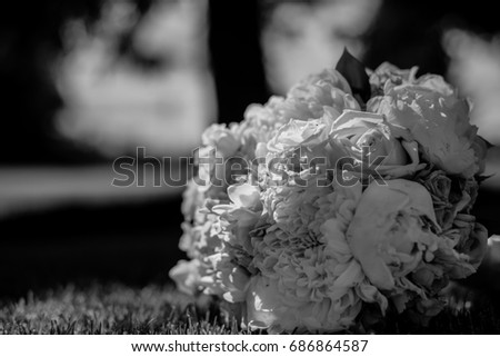 Picture of a wedding bouquet , Wedding bouquet of pink and white roses / white and yellow flowers with green, decorated with silk ribbons, lie on the grass. The bride's bouquet. Black and white photo