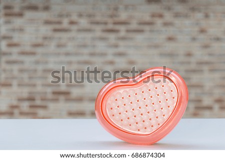 Pink plastic heart on white wood and blurred wall background
