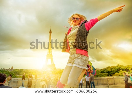 Happy tourist woman jumping with Tour Eiffel on background. Lifestyle traveler enjoing at Eiffel Tower from Place du Trocadero, icon of Paris, France. Freedom and travel concept. Sunset dramatic sky.